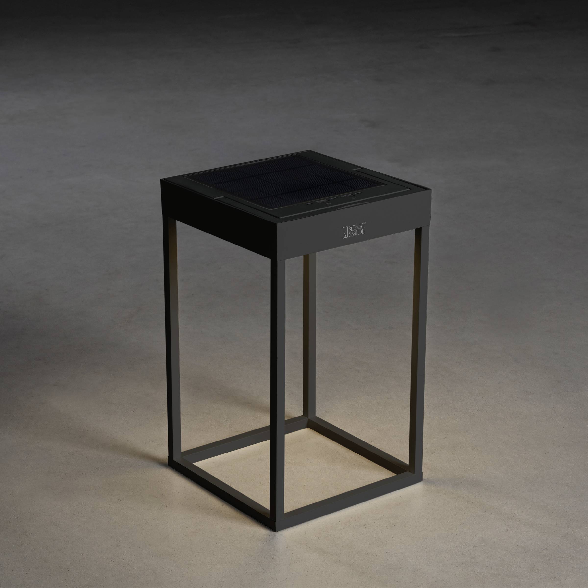 Une table d'appoint moderne, carrée, noire avec un cadre métallique minimaliste est posée sur un sol gris.