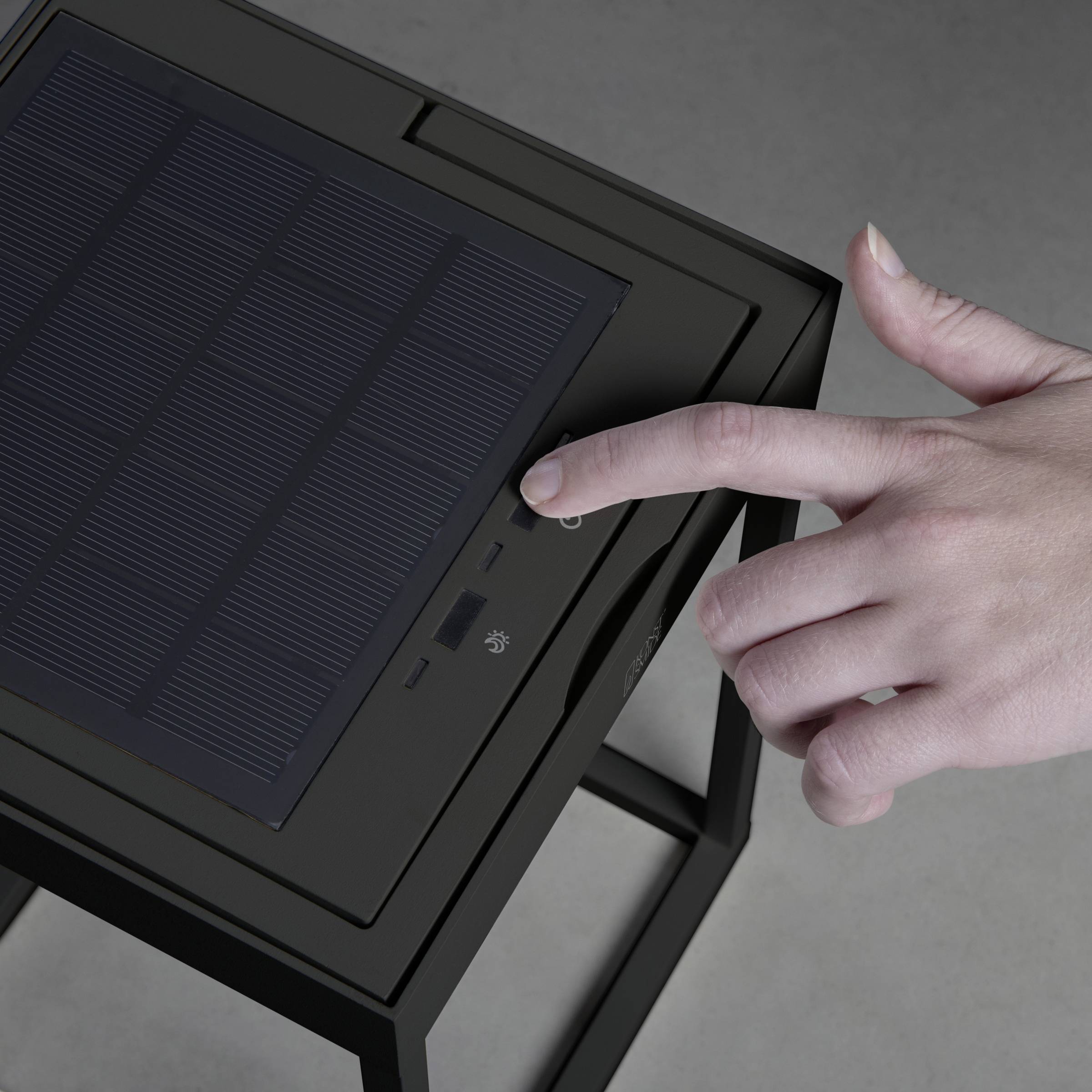 Une main pointe un panneau solaire sur un appareil compact posé sur une table.