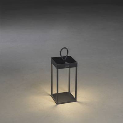 Une lanterne noire en métal avec une poignée est posée sur un sol. Elle brille de l'intérieur et projette une lumière douce.