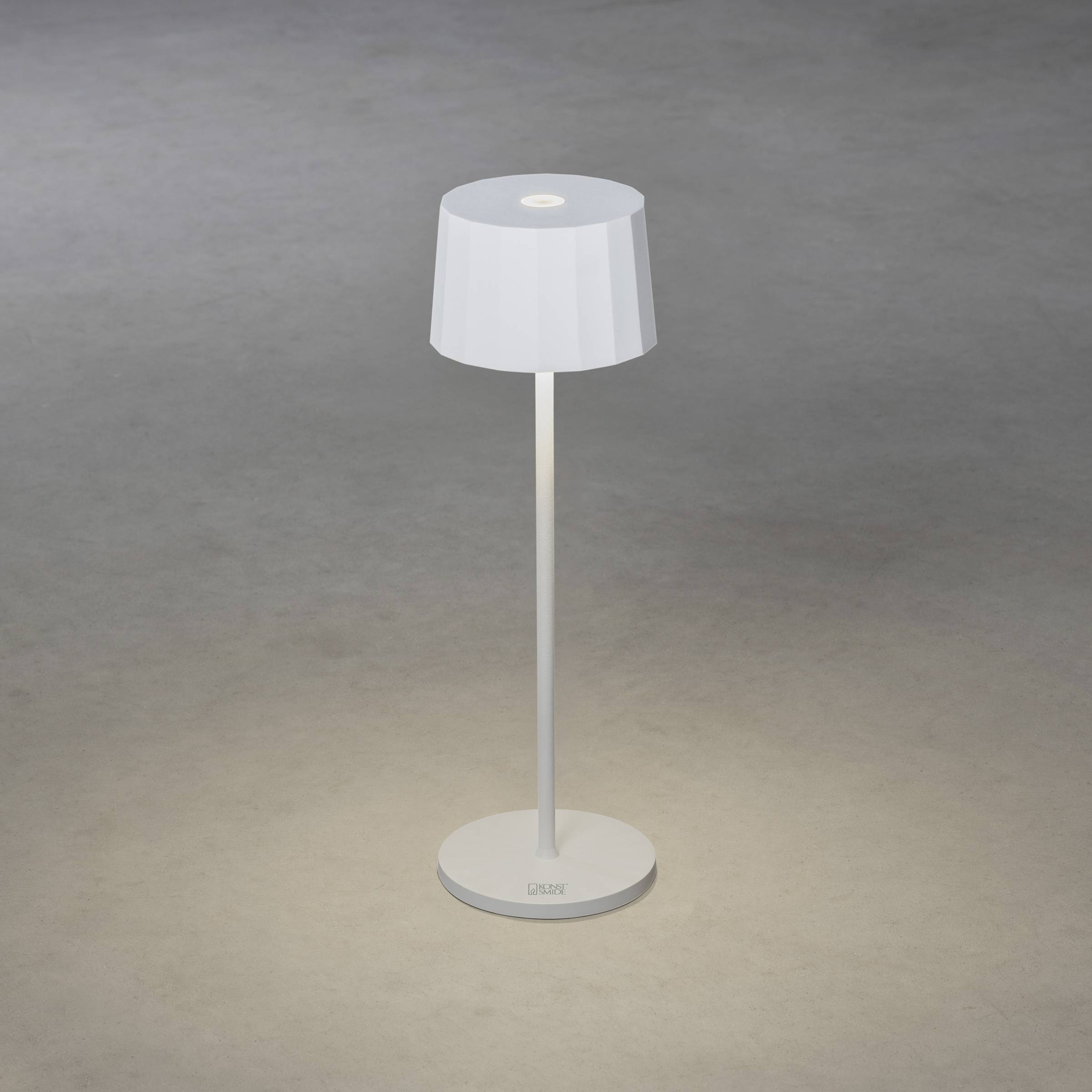 Lampe de table blanche sur un fond gris, illuminant sa base. Elle présente un design simple et moderne.