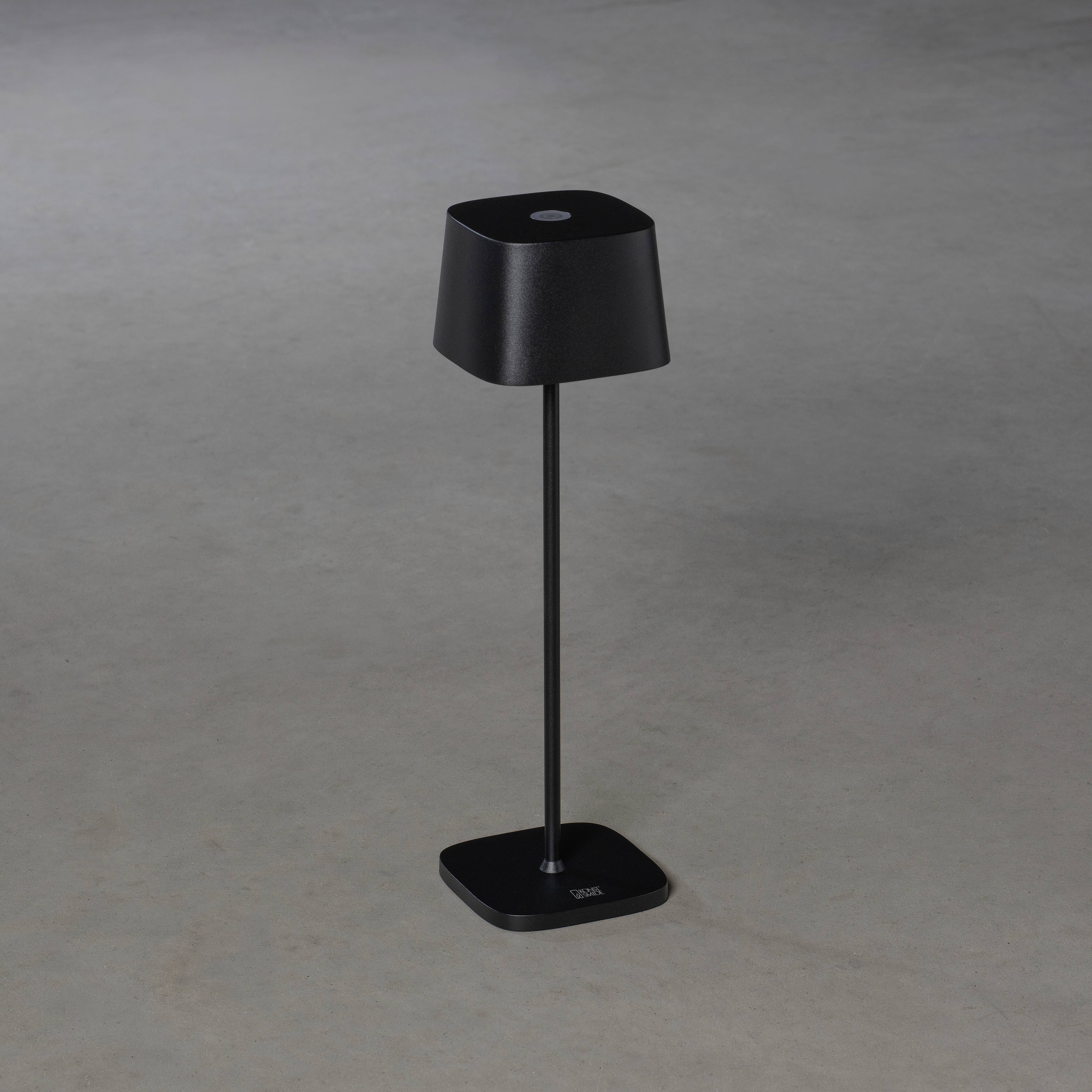 Lampe de table noire avec un pied élancé et un abat-jour carré sur fond gris.