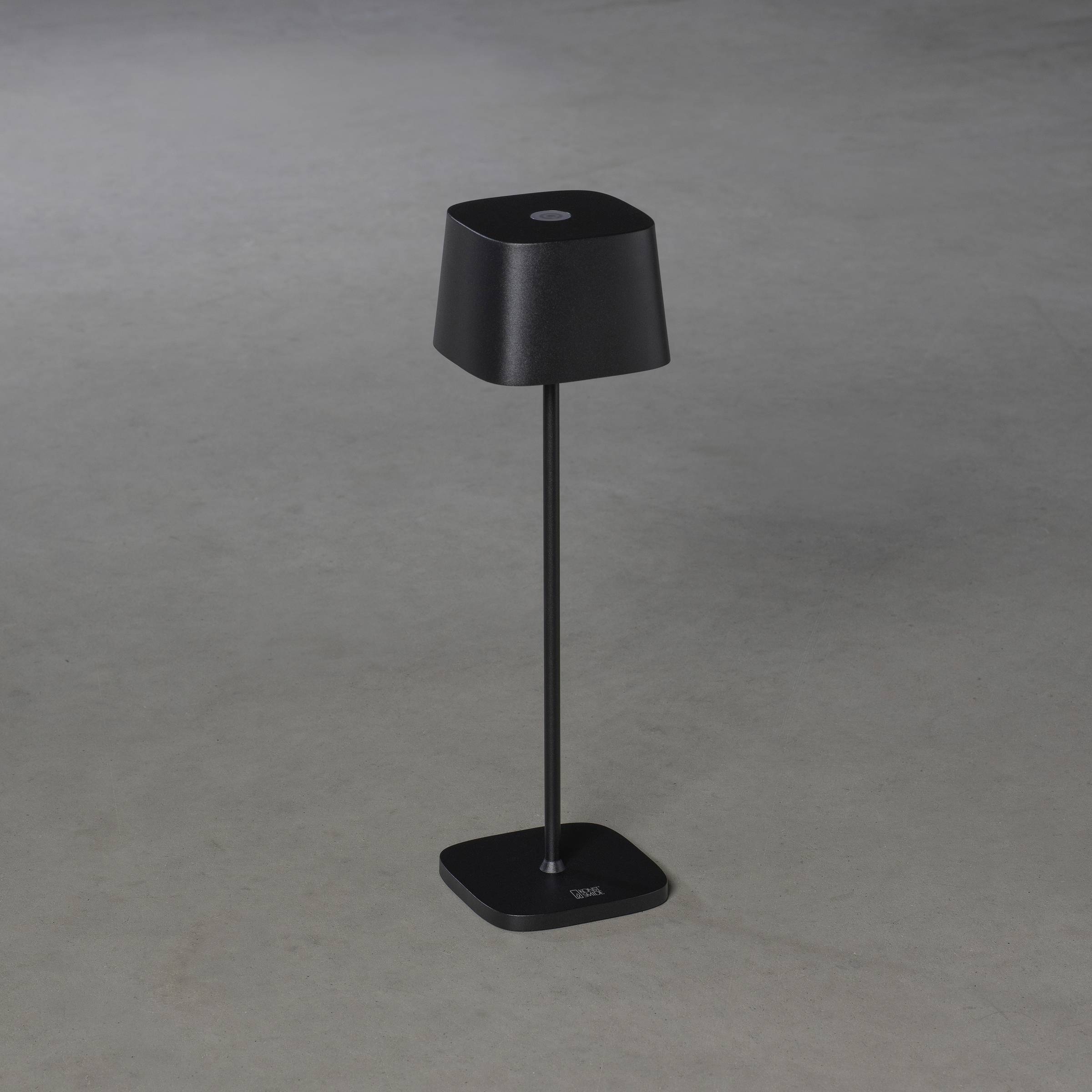 Une lampe sur pied noire et moderne avec un abat-jour carré est posée sur un sol gris.