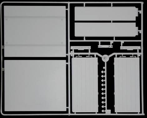Kit de modélisme plastique avec des pièces rectangulaires sur un cadre, sur un fond noir. Les pièces semblent non assemblées et triées.