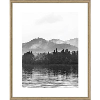 Photographie en noir et blanc d'un lac tranquille avec des arbres et des collines en arrière-plan, ambiance brumeuse, paysage paisible.