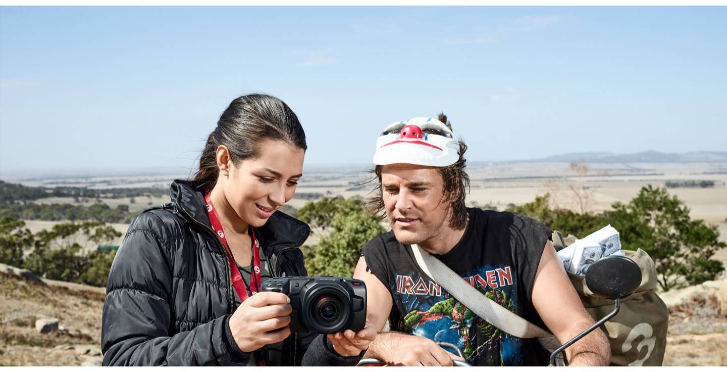Une femme montre une caméra à un homme portant un casque dans un environnement paysager. Tous deux regardent l'écran de la caméra.