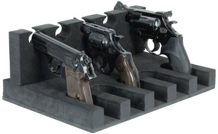 Trois pistolets disposés dans un support en mousse noire, chacun placé dans un compartiment séparé sur une table.