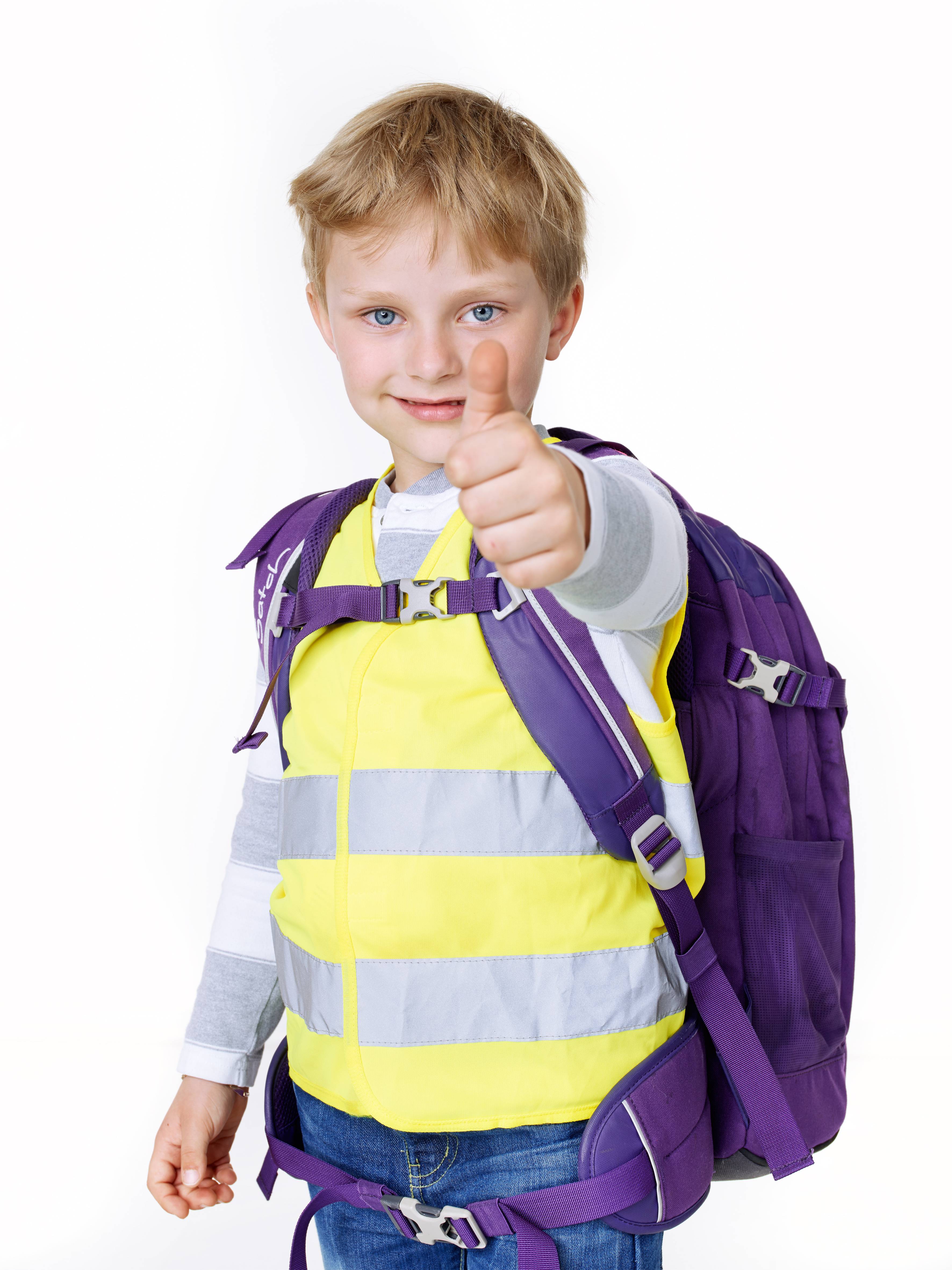 Un garçon portant un gilet de sécurité jaune et un sac à dos violet fait un signe de pouce levé.