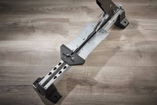 Un support de sol en argent sur un plancher en bois. Le support comporte plusieurs rangées de trous et des bouchons en plastique noir aux extrémités.