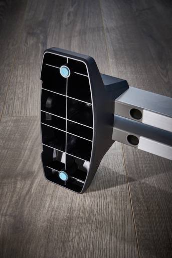 Support en plastique noir avec des boutons bleus posé sur un plancher en bois. Pièce d'un assemblage de meuble.