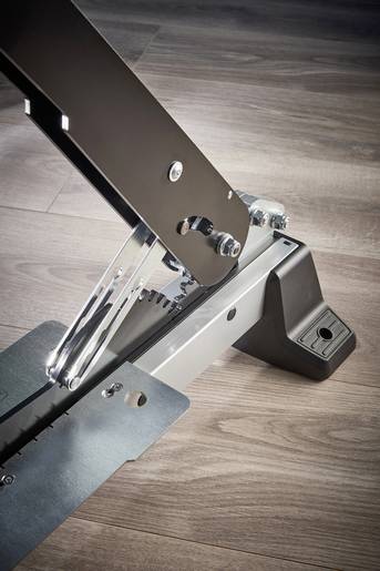 Mécanisme métallique sur plancher en bois, montrant des pièces métalliques assemblées avec des vis et des leviers.