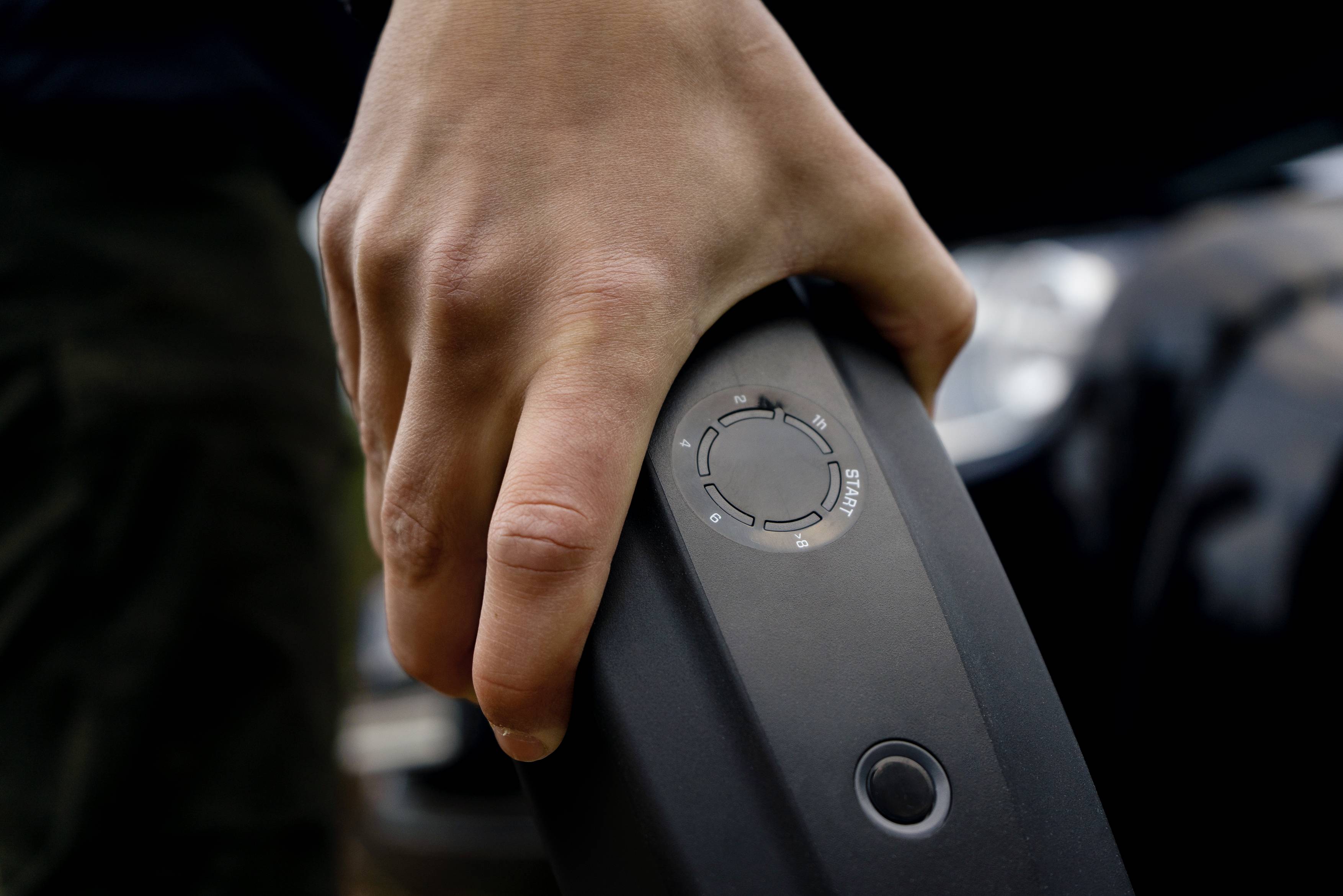 Une main tient une batterie de vélo électrique. Sur la batterie se trouve un indicateur de charge avec un diagramme circulaire.