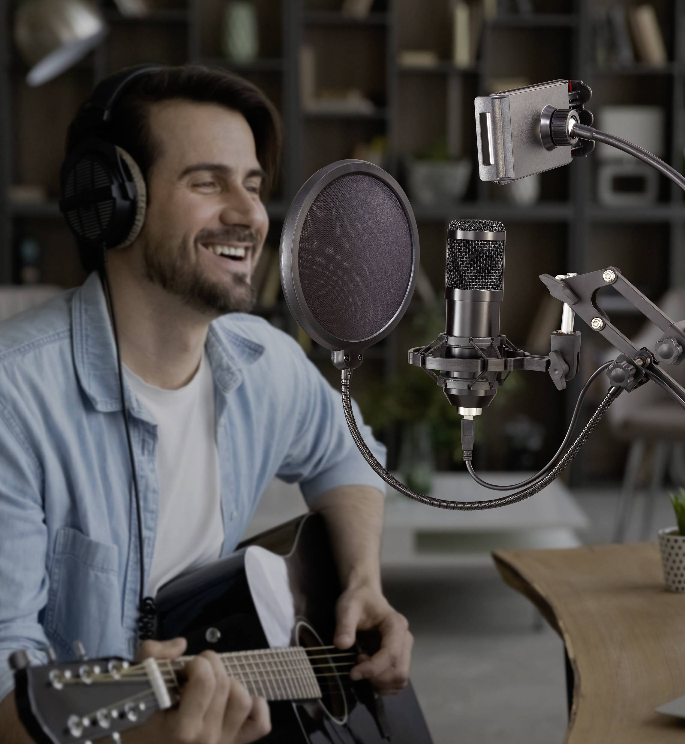 Un homme est assis avec des écouteurs et joue de la guitare devant un microphone. Il sourit pendant qu'il est enregistré.