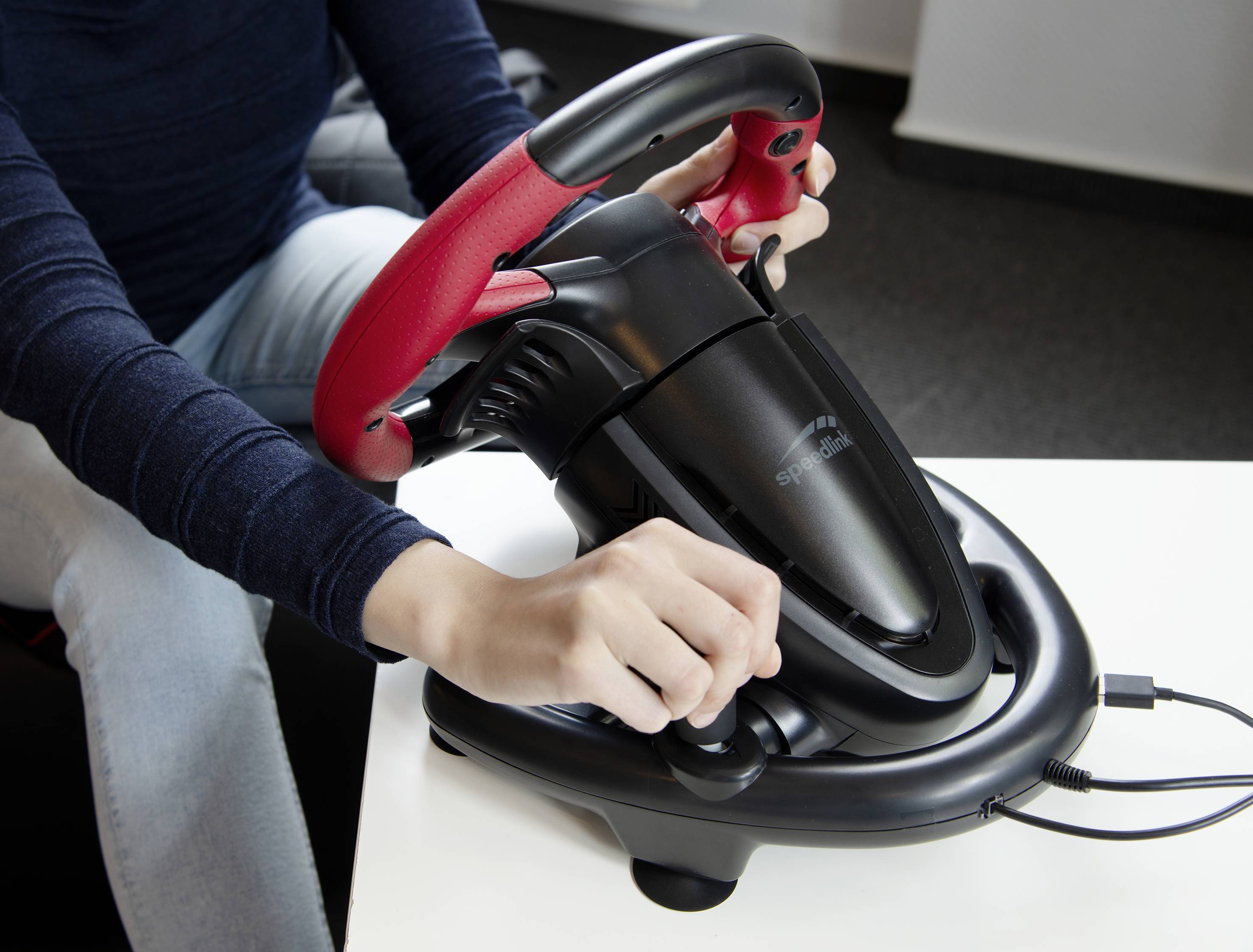 Une personne utilise un volant de contrôle noir et rouge sur une table.