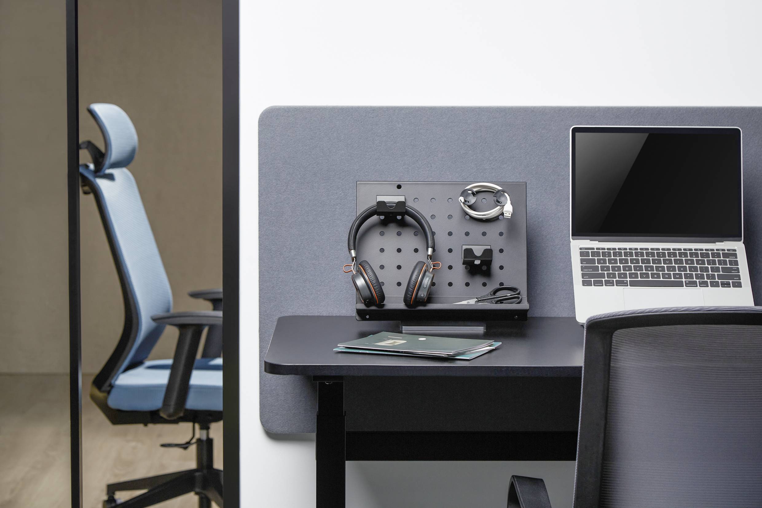 Poste de travail avec un ordinateur portable sur une table, des écouteurs posés sur un support à côté. Un fauteuil de bureau vide est visible en arrière-plan.