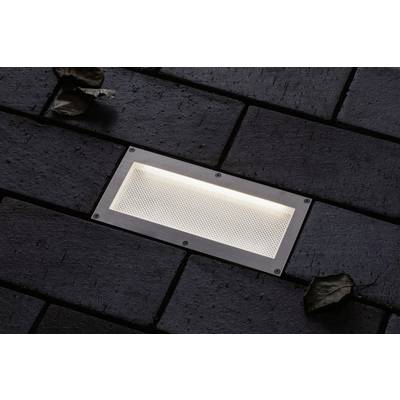 Lampe de sol illuminée dans un pavage sombre, entourée de feuilles.