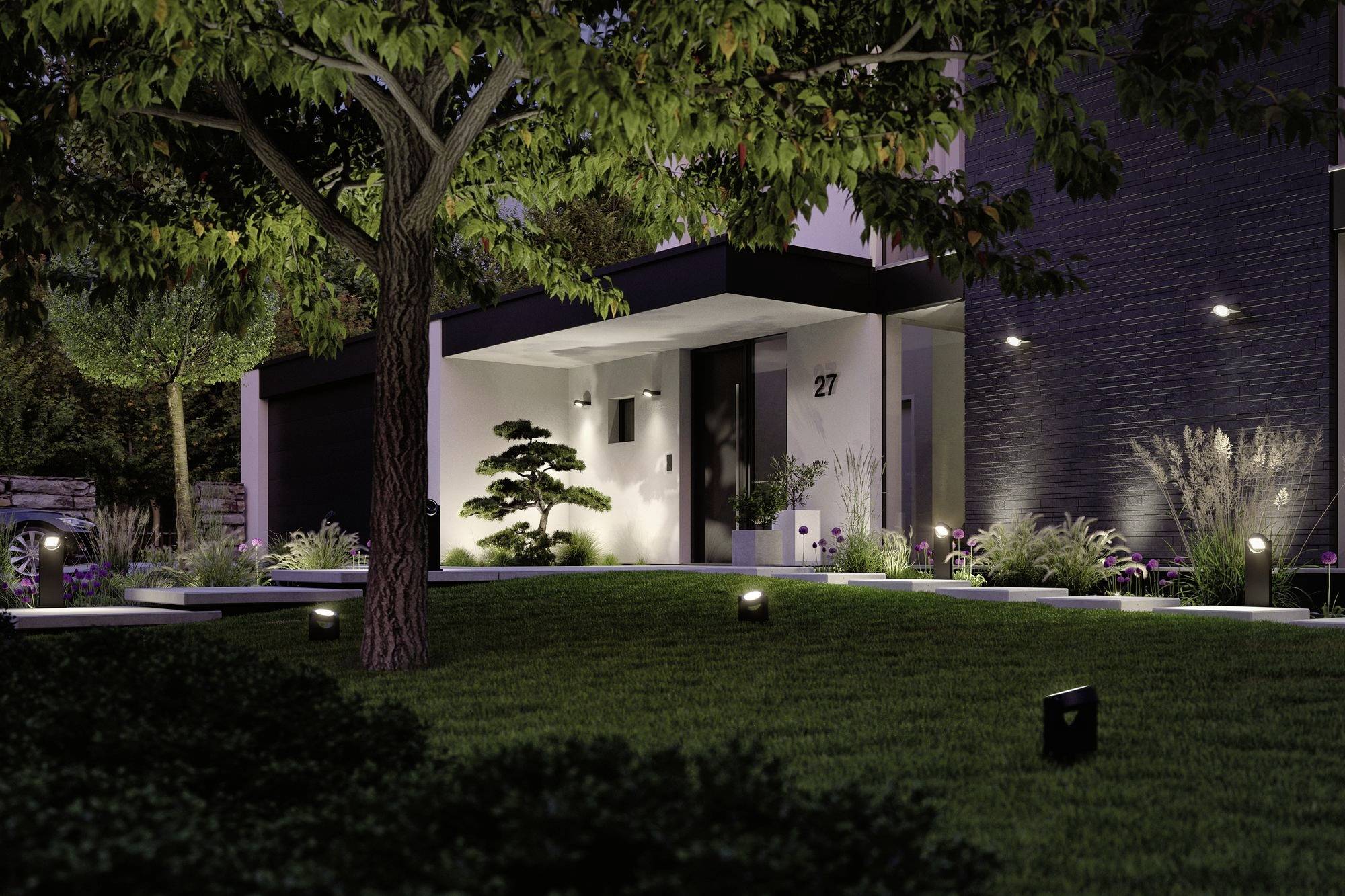Une maison moderne la nuit, éclairée par des lumières de jardin. Le jardin avant est soigneusement entretenu avec des arbres et des arbustes. Le numéro 27 est visible.