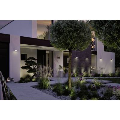 Façade de maison moderne au crépuscule avec un jardin éclairé, des formes géométriques épurées et un aménagement paysager soigné.