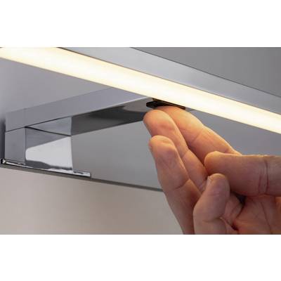 Une main appuie sur l'interrupteur d'un luminaire LED moderne et rectangulaire fixé au mur. La lampe diffuse une lumière chaleureuse.