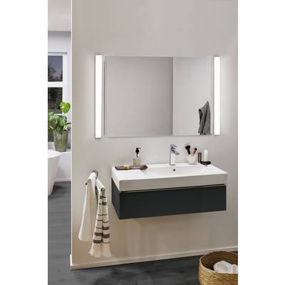 Une salle de bain moderne avec un lavabo, un grand miroir et des serviettes ; à gauche une fenêtre avec des plantes ; à droite un panier.