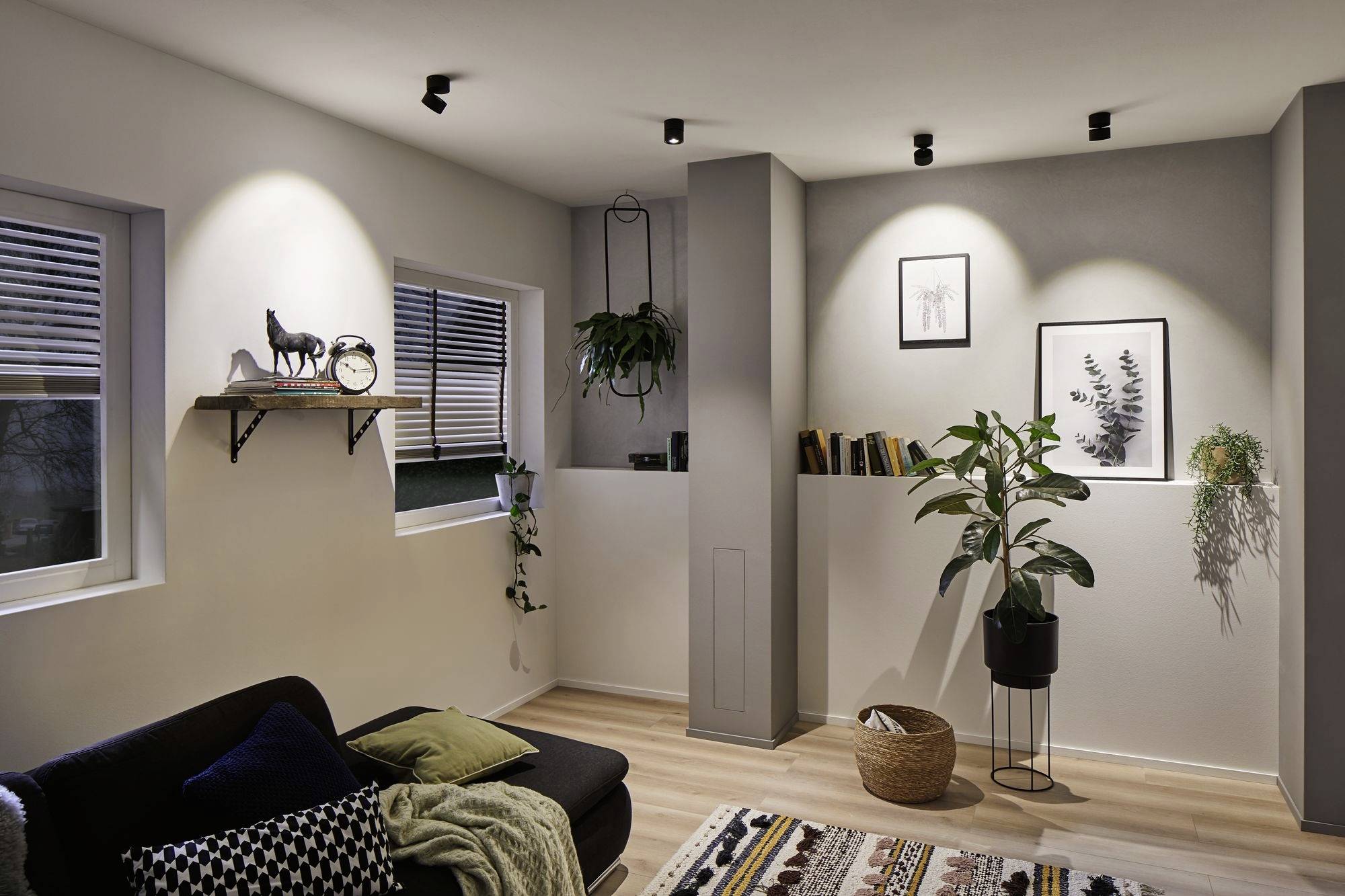 Un salon élégamment aménagé avec un éclairage chaleureux. Des plantes, des tableaux et des objets décoratifs sur une étagère créent une atmosphère accueillante.
