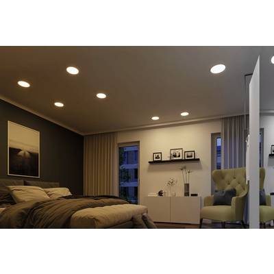 Chambre à coucher avec un lit double, un fauteuil confortable et des photos accrochées au mur. Des luminaires au plafond diffusent une lumière chaleureuse.