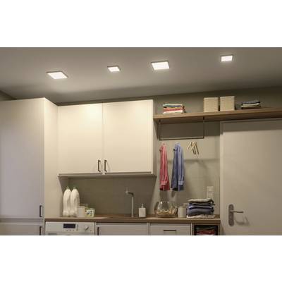 Cuisine avec un placard suspendu, chemises accrochées au mur, étagères avec des serviettes pliées et deux cruches de lait posées sur une machine à laver.