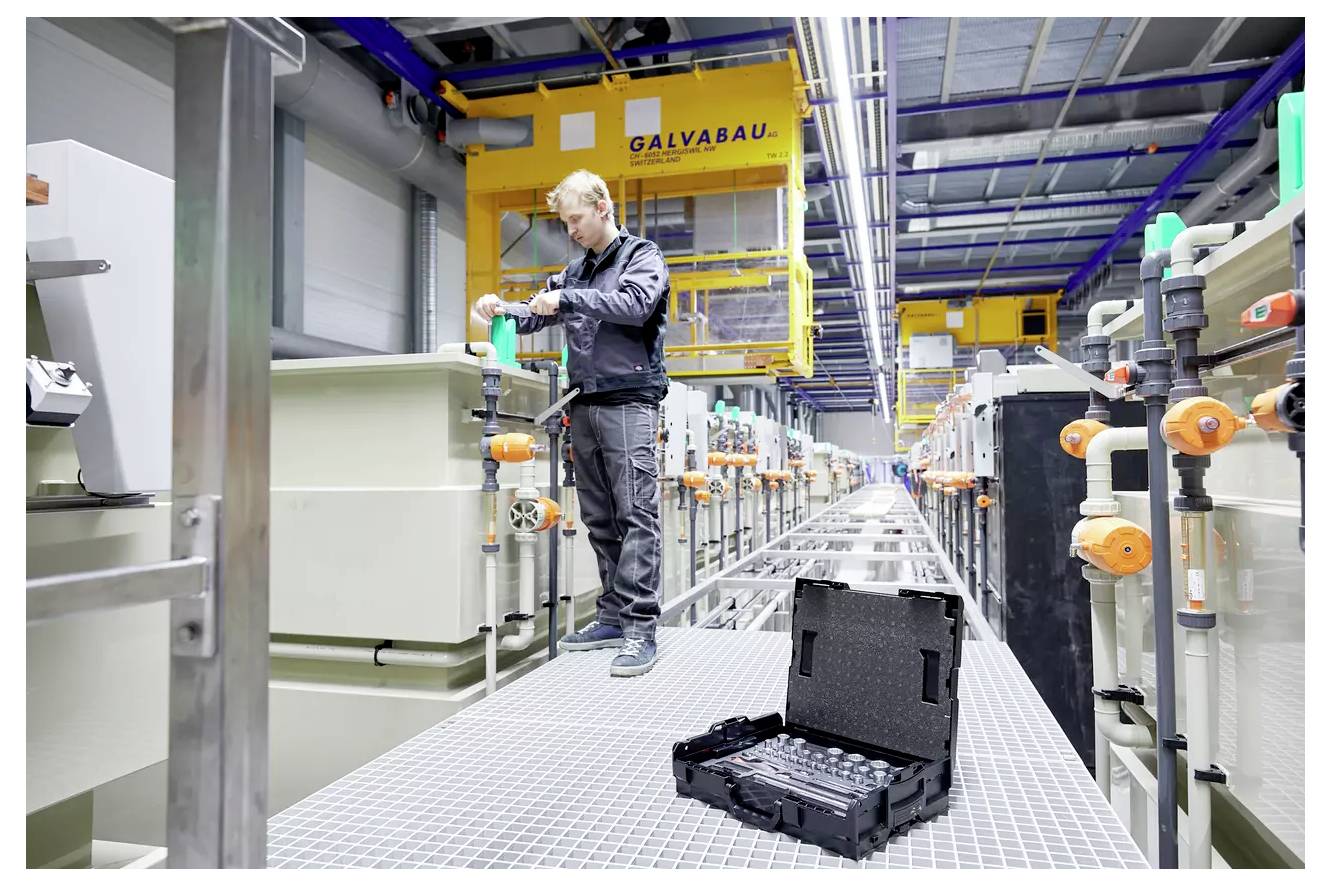 Un technicien dans un atelier fait fonctionner des machines sur une passerelle industrielle, avec de l'équipement et des outils au premier plan, créant un environnement de travail chargé.