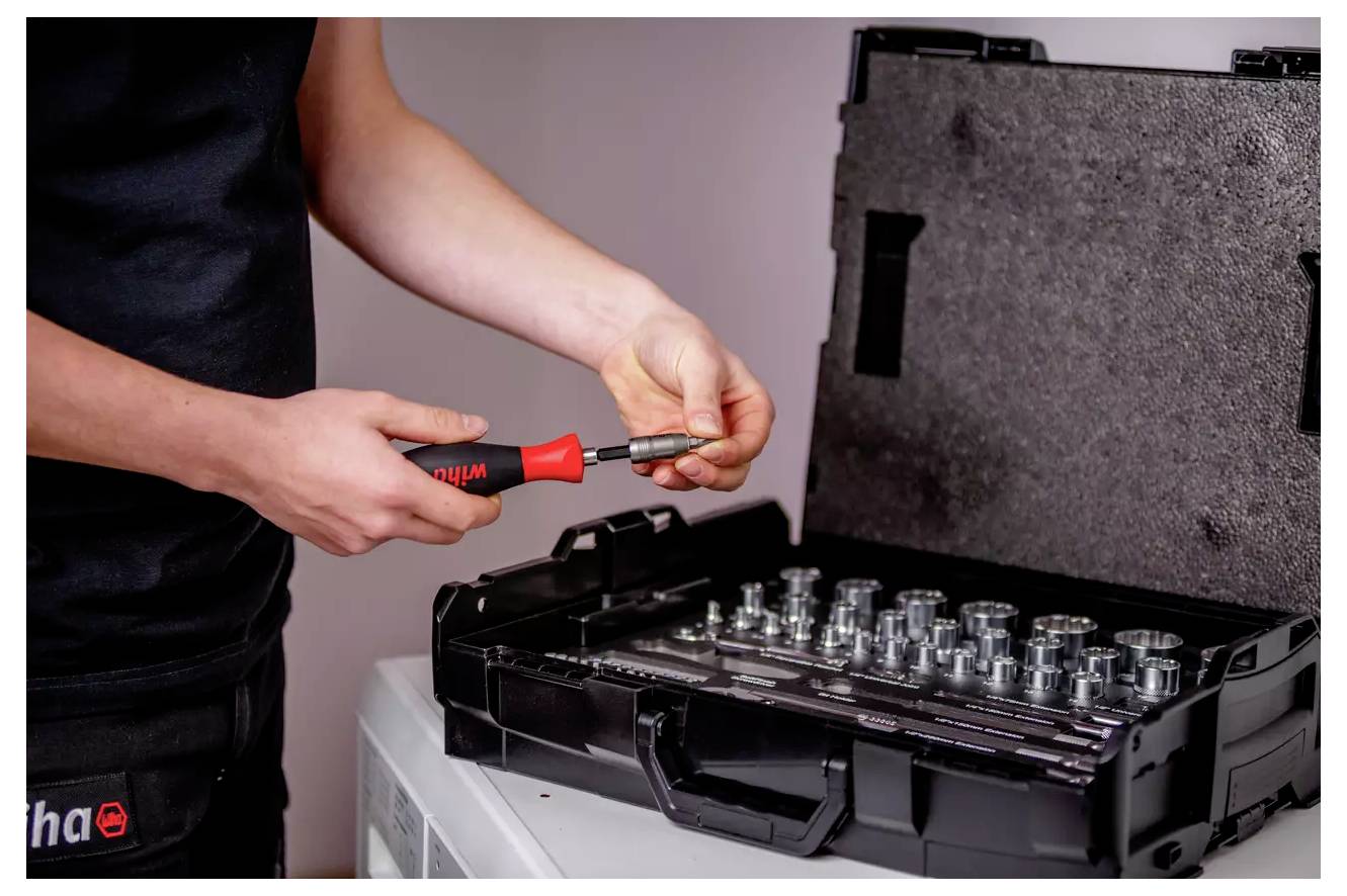 Une personne ajuste un outil provenant d'une boîte à outils, qui comprend diverses pièces de douilles dans un étui noir, possiblement pour des travaux mécaniques.