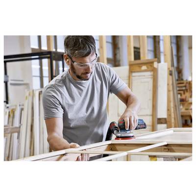 Une personne portant des lunettes de sécurité et une protection auditive utilise une ponceuse électrique sur un cadre en bois dans un environnement d'atelier.