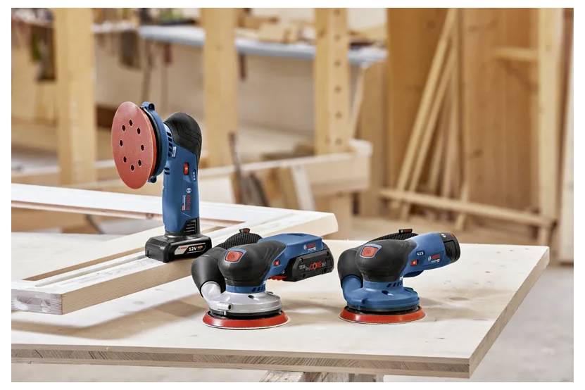 Trois ponceuses portatives avec des designs bleu et noir sont placées sur une surface en bois dans un environnement d'atelier.