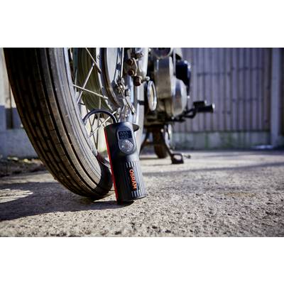 Un manomètre numérique de pression des pneus est posé sur le sol à côté d'un pneu de moto et affiche la pression d'air.