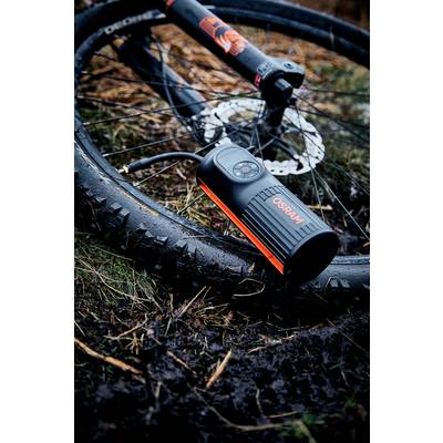 Pneu de vélo avec pompe à air comprimé dans un environnement humide. Un VTT est posé au sol, la pompe est marquée 'OSRAM'.