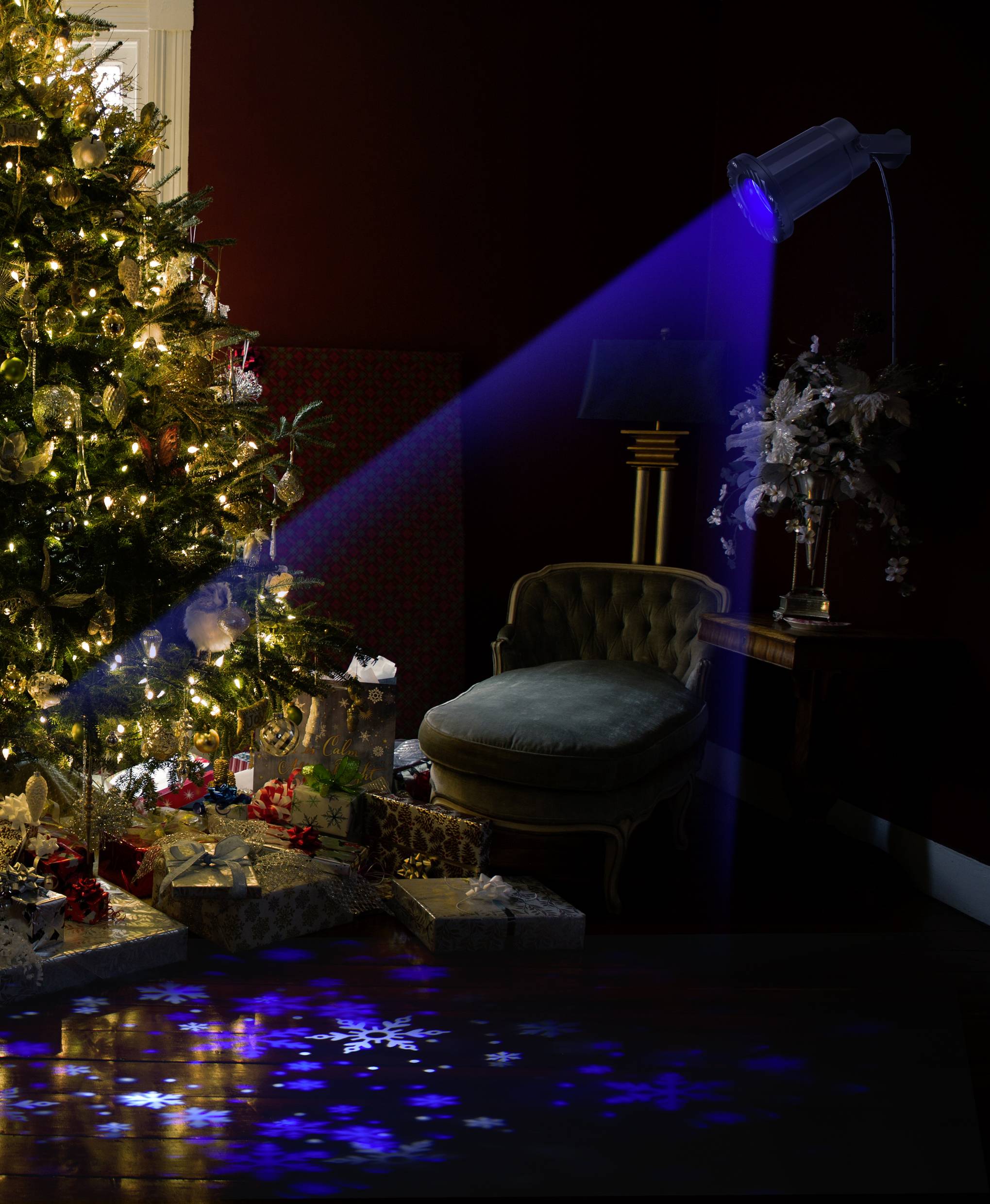 Un sapin de Noël magnifiquement décoré se trouve dans un salon. Un projecteur bleu projette des motifs de flocons de neige sur le sol.