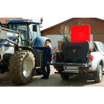 Un homme se tient entre un tracteur bleu et un pick-up blanc avec un réservoir de carburant sur la benne. Des bâtiments agricoles sont visibles en arrière-plan.