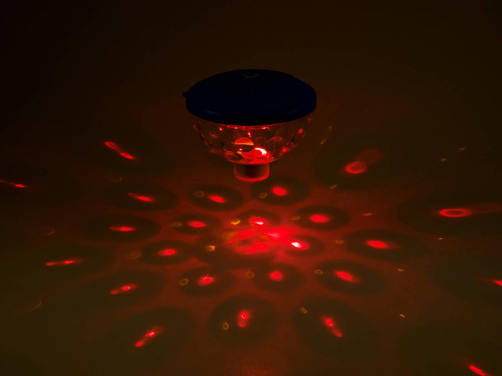 Un appareil éclairé en rouge projette un motif circulaire de points et d'ovales rouges sur une surface sombre.