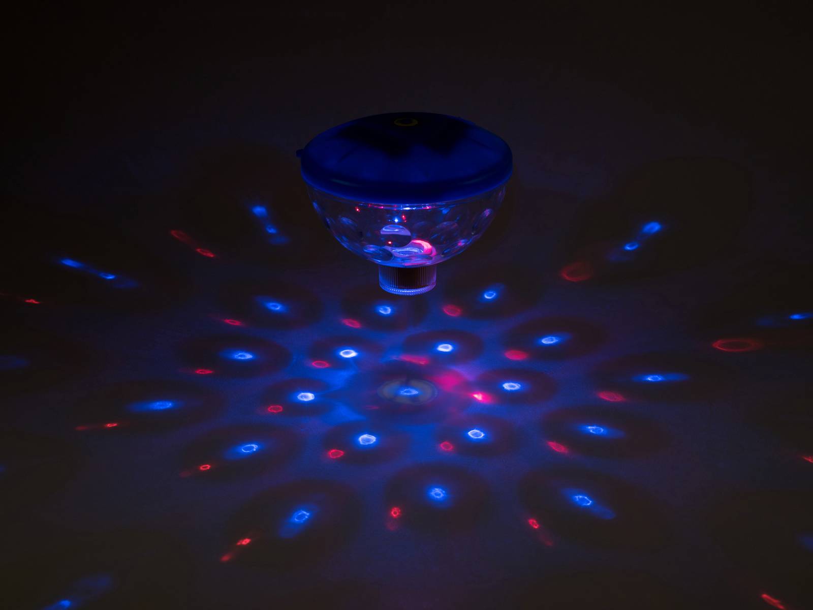 Une lampe LED lumineuse projette un motif de points lumineux rouges et bleus dans une pièce sombre.