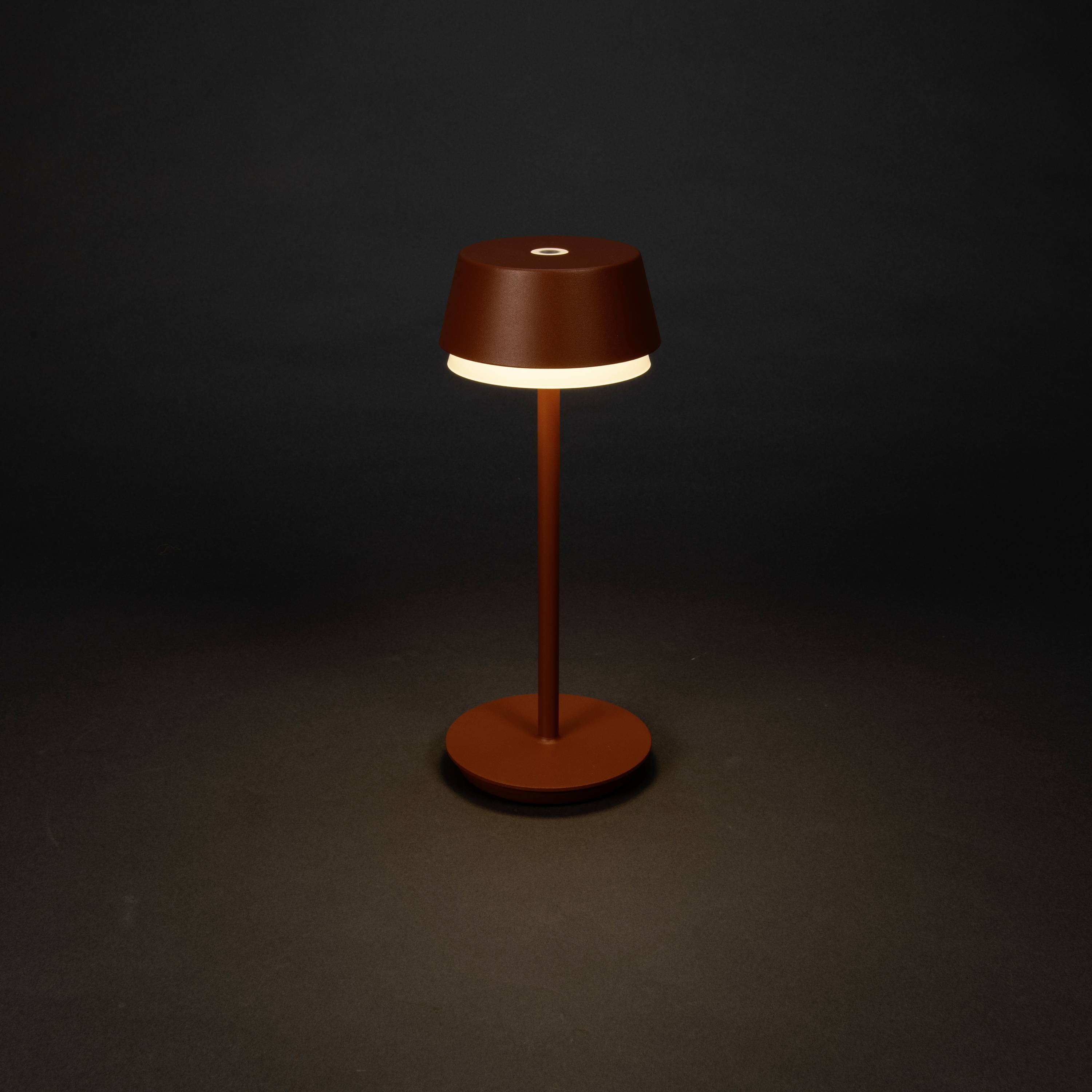 Une lampe de table moderne au design minimaliste, dotée d'un abat-jour et d'un socle ronds, diffuse une lumière chaleureuse sur un fond sombre.