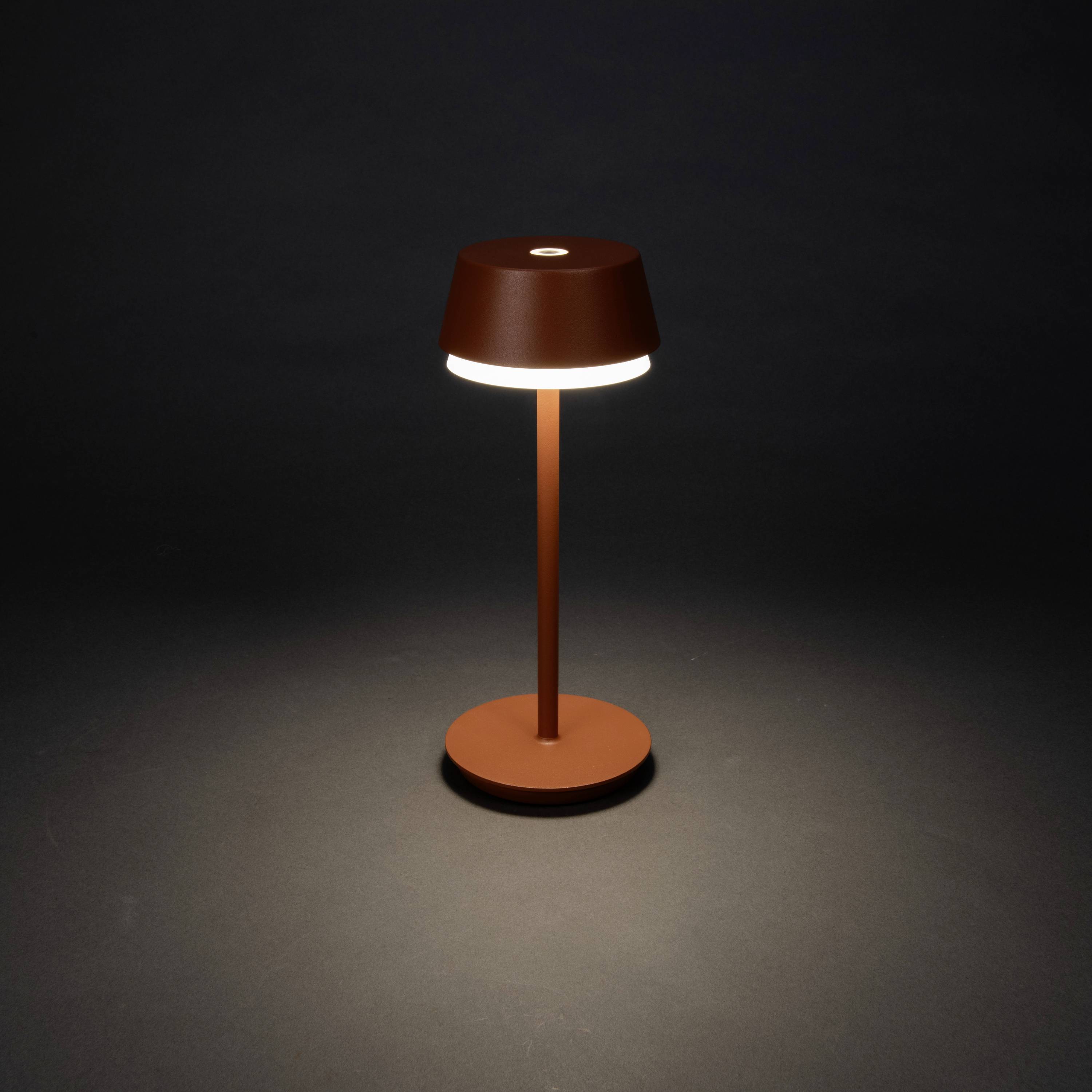 Une lampe de table élégante avec un abat-jour rond qui diffuse une lumière douce vers le bas, posée sur un fond sombre.