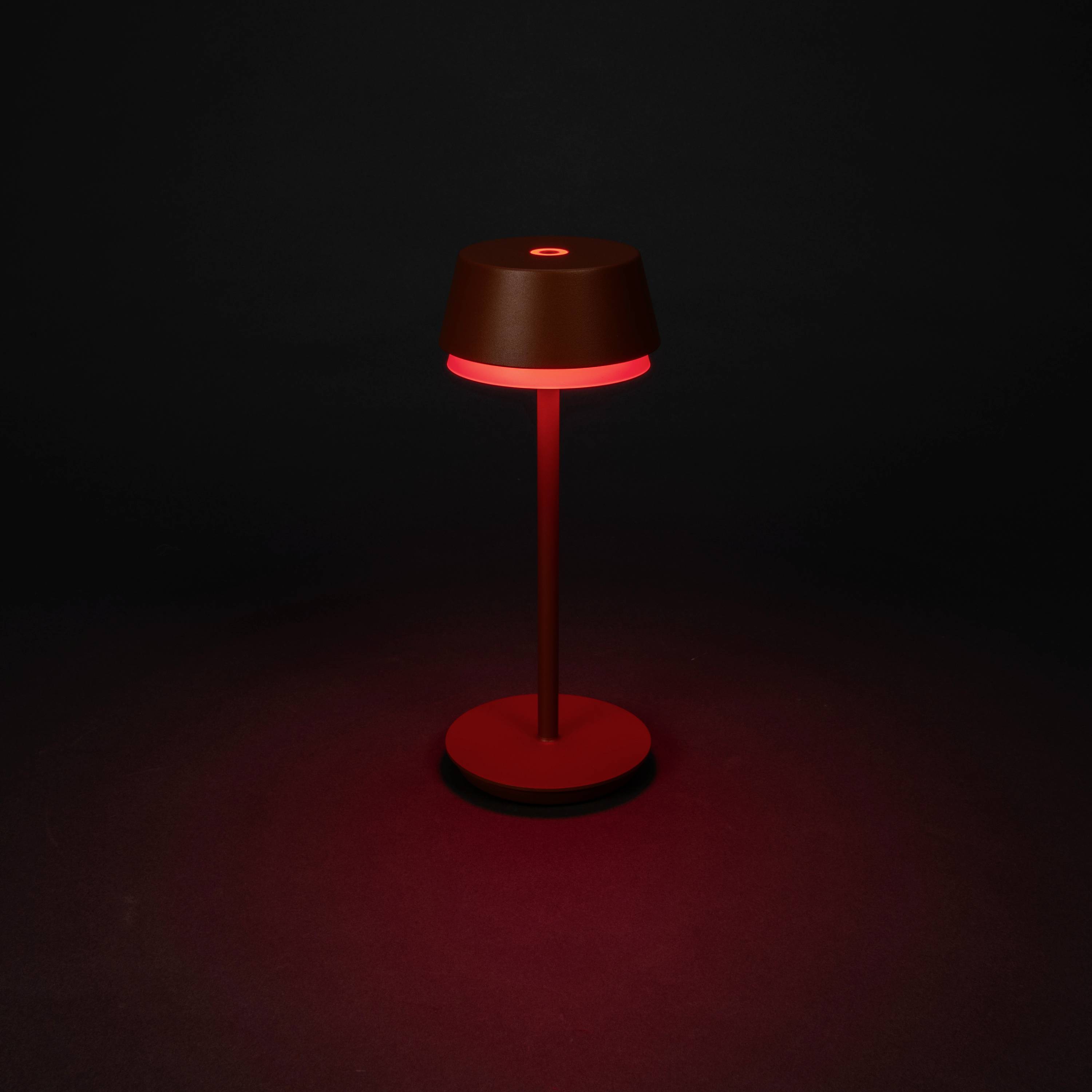 Une lampe de table rouge éclaire une pièce sombre et diffuse une lumière chaleureuse qui crée une atmosphère accueillante.