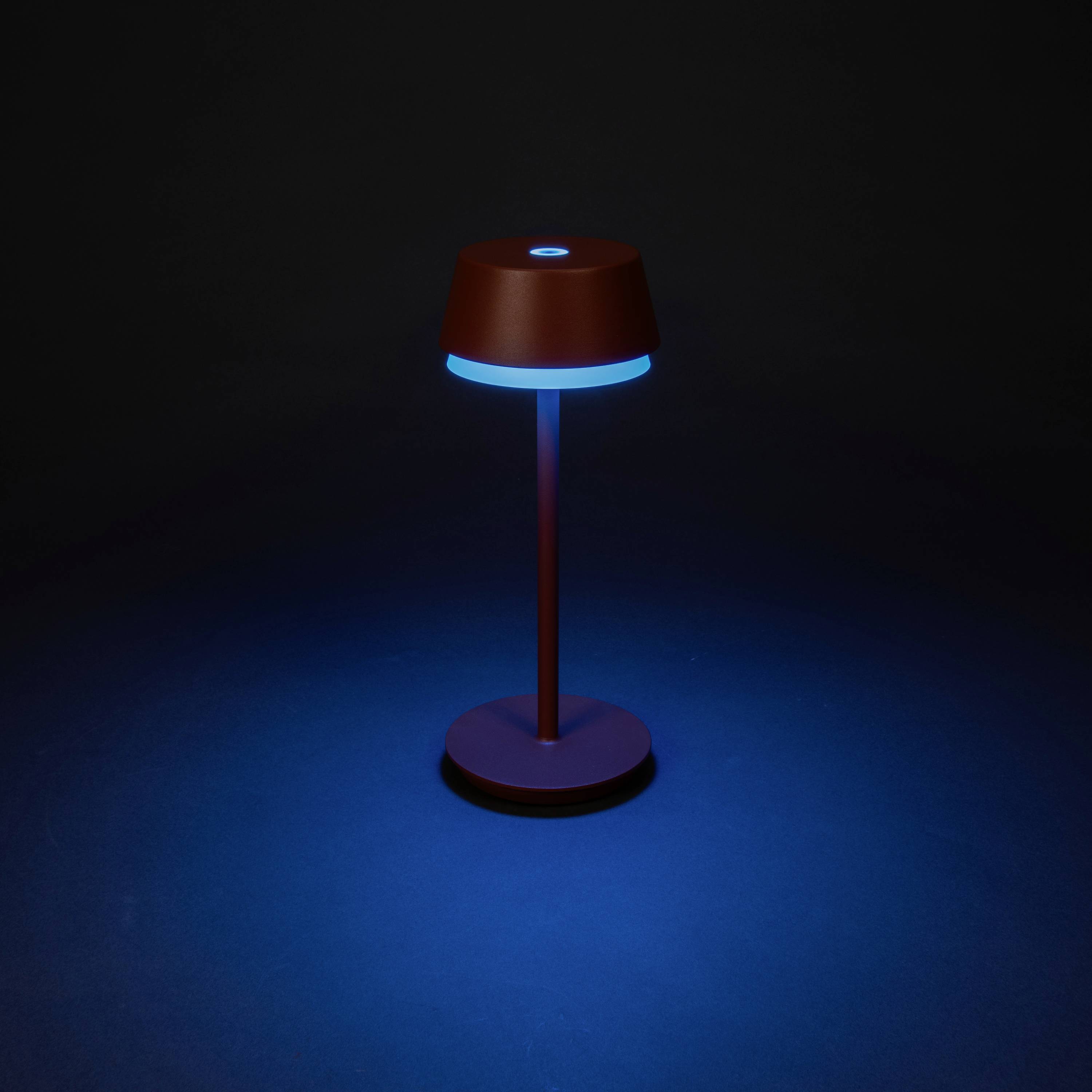 Une lampe de table élégante et moderne, émettant une lumière bleue qui crée une atmosphère calme et intimiste dans une pièce sombre.