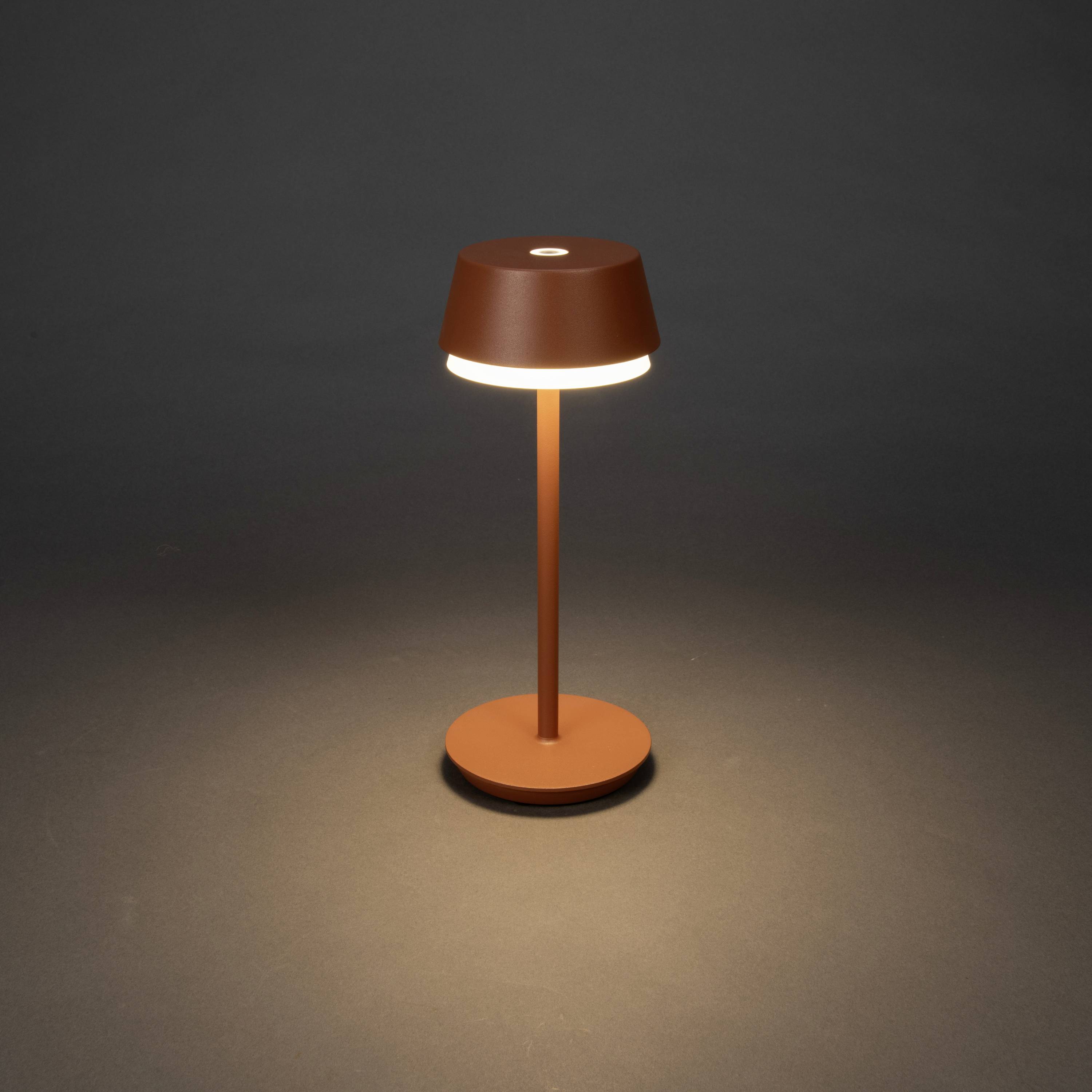 Une lampe de table minimaliste à abat-jour brun s'illumine sur un fond sombre.