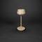 Une lampe de table minimaliste beige sur un fond sombre. Elle a un abat-jour rond et une tige élancée reposant sur une base circulaire.