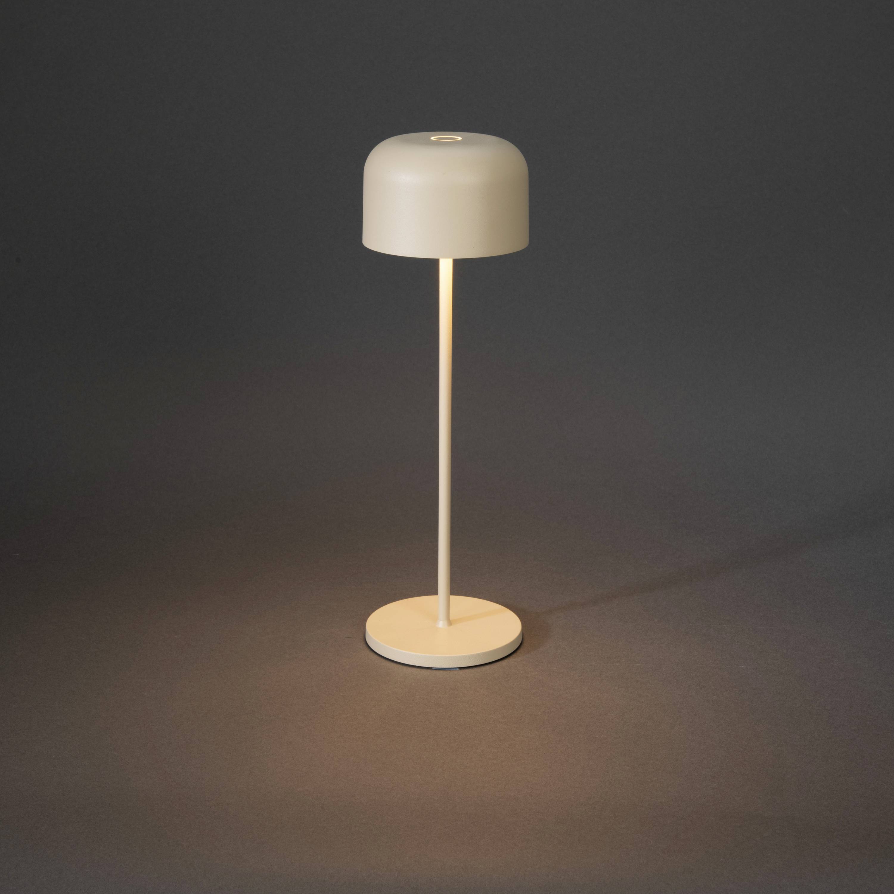 Une lampe de table simple et moderne avec un abat-jour cylindrique lumineux sur un pied étroit, posée sur un fond sombre.