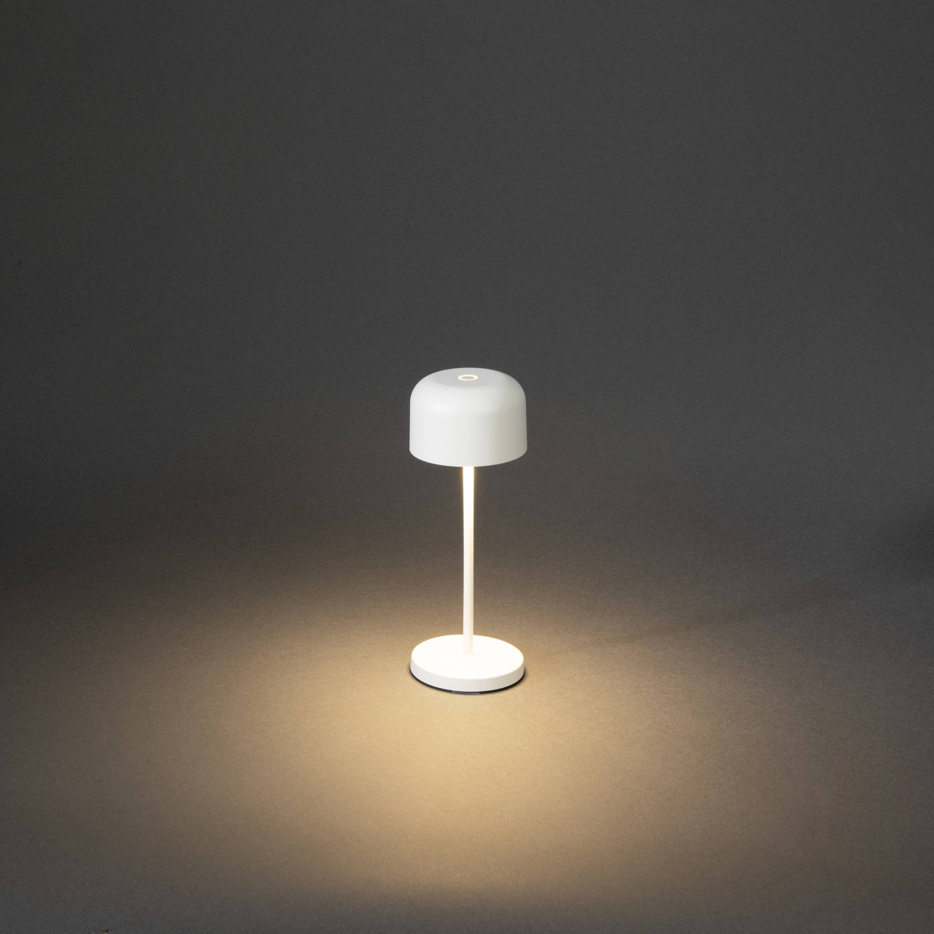Une petite lampe de table moderne avec un abat-jour rond blanc éclaire un arrière-plan sombre.