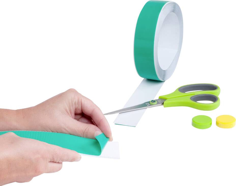 Des mains coupent du ruban adhésif vert avec des ciseaux verts. À côté, deux aimants colorés sont posés.