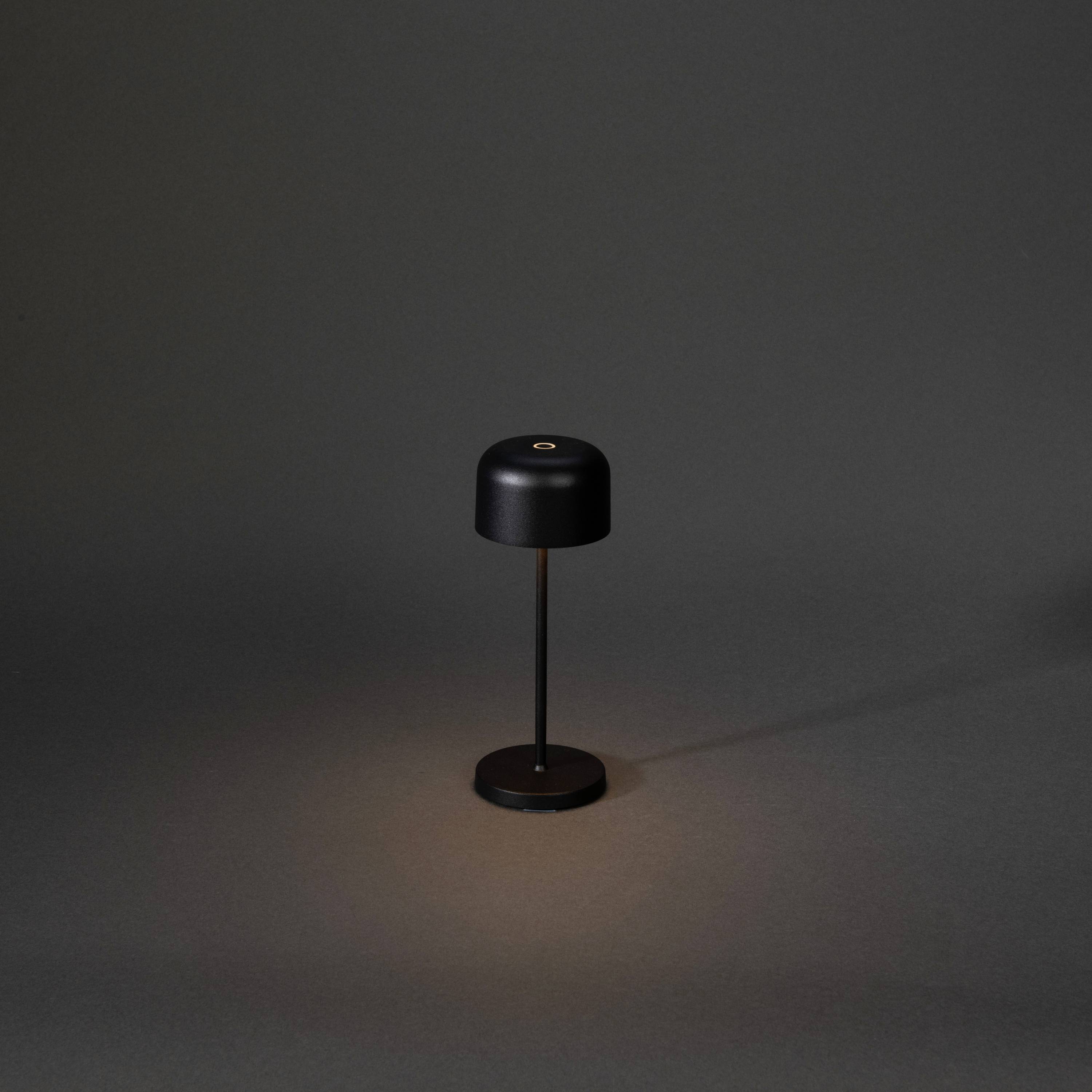 Une lampe de table minimaliste en noir projetant un cône de lumière doux sur une surface sombre en arrière-plan.