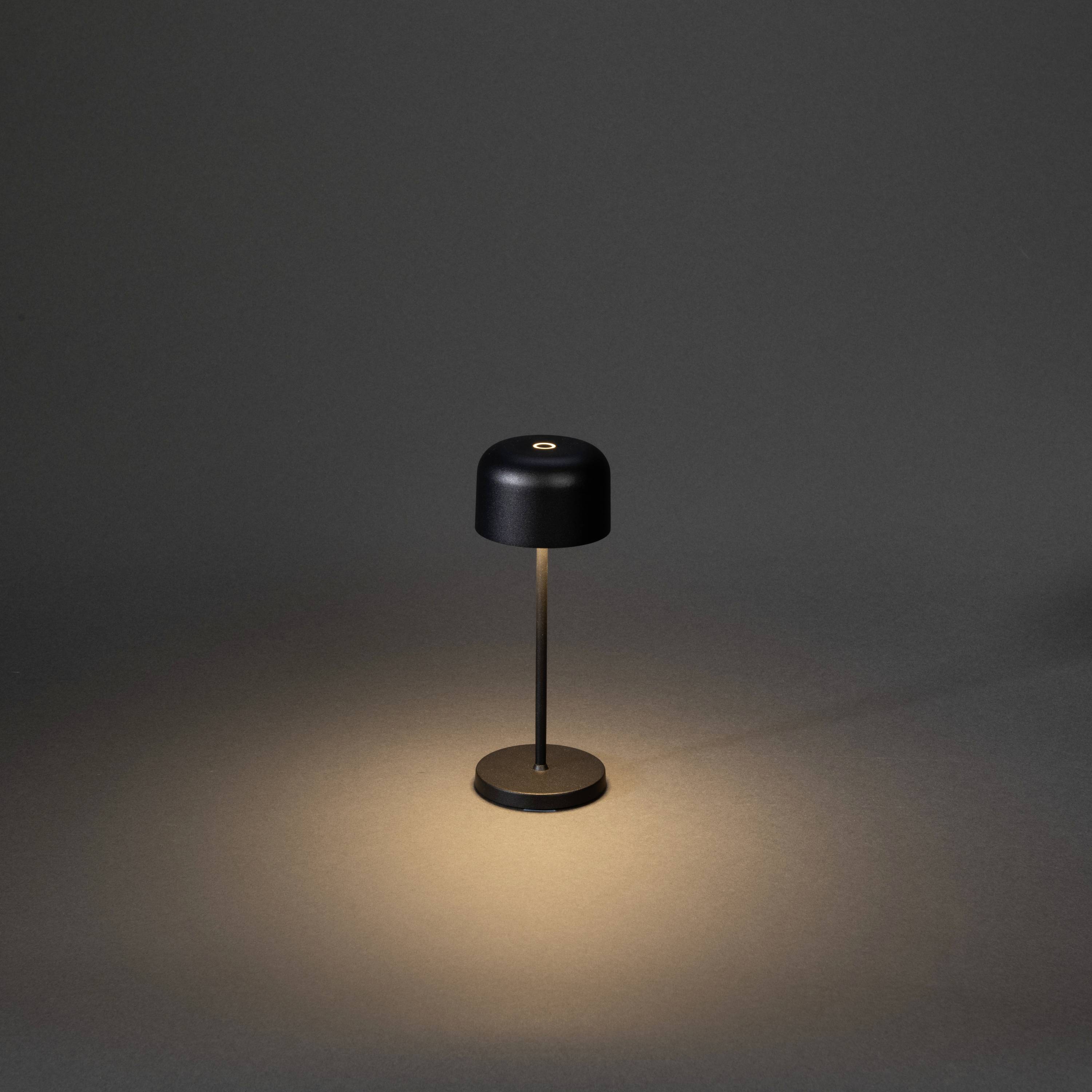 Une lampe de table noire s'illumine sur un fond sombre. Elle arbore un style minimaliste et projette un cône de lumière chaleureux.