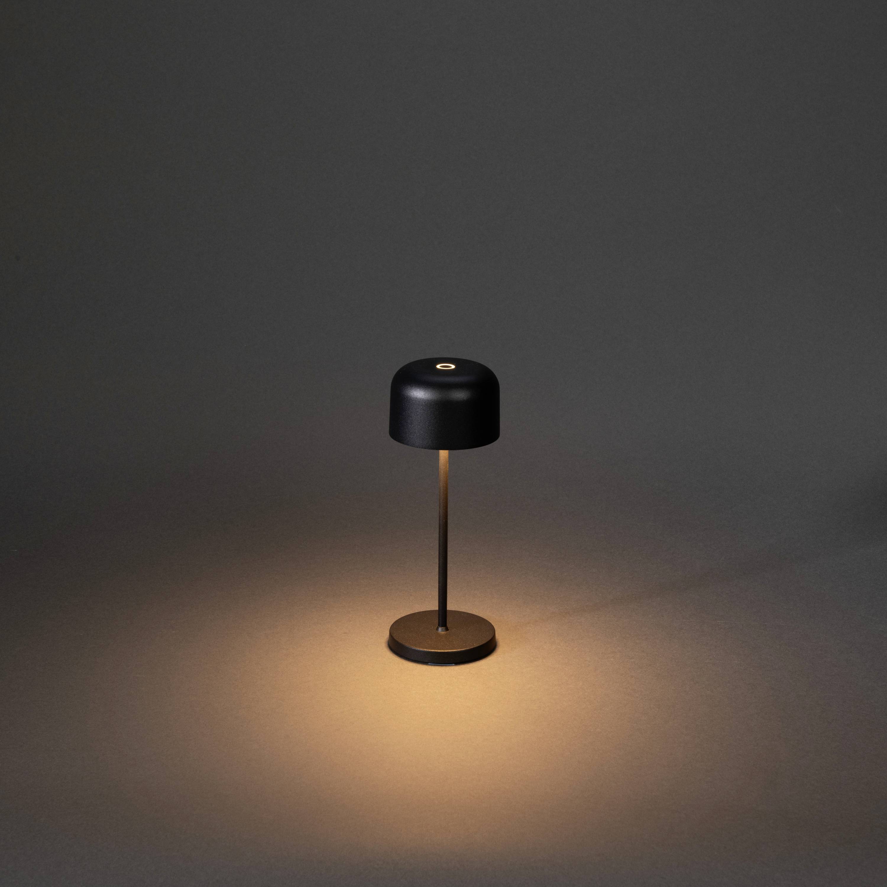 Une lampe de table minimaliste noire diffuse une lumière chaleureuse sur un fond sombre.