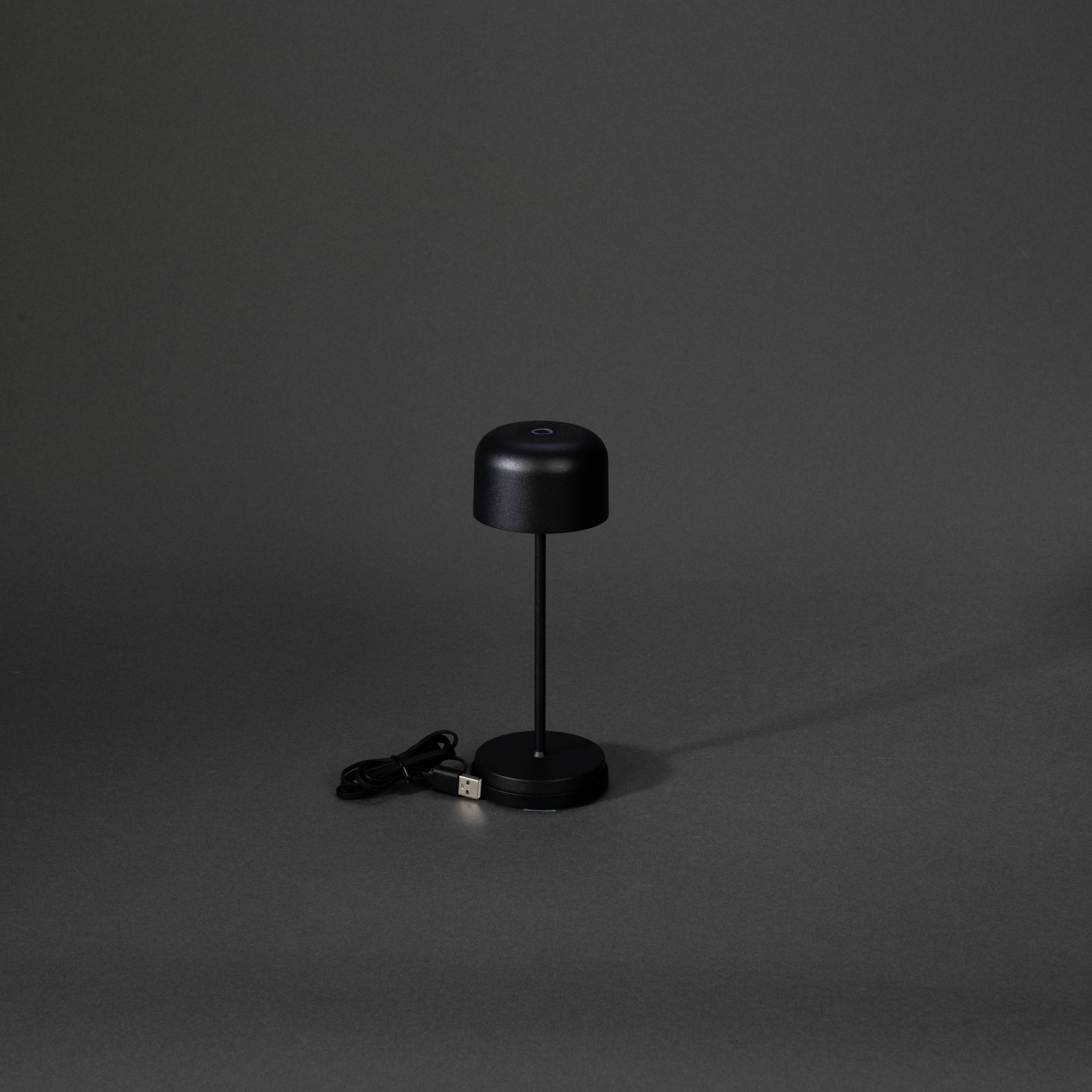 Une lampe de table noire, minimaliste, avec un abat-jour rond et un câble USB, repose sur un fond sombre.