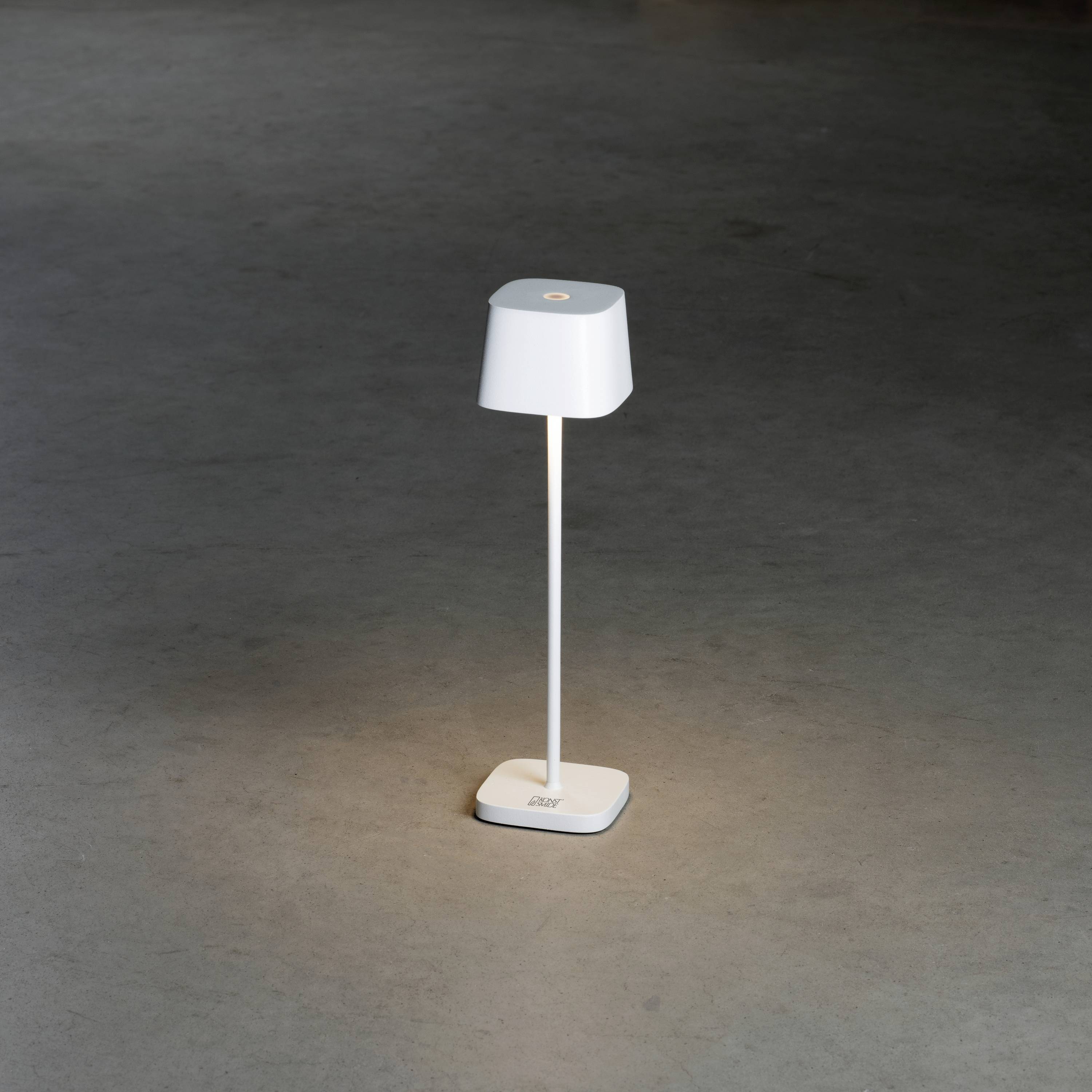Une lampe de table blanche est posée sur un sol gris, illuminant la zone directement en dessous d'elle.